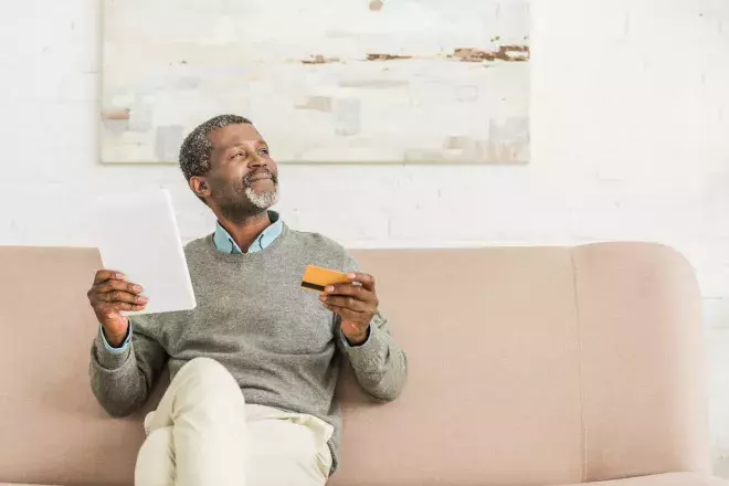 smiling man sitting on couch with credit card and phone