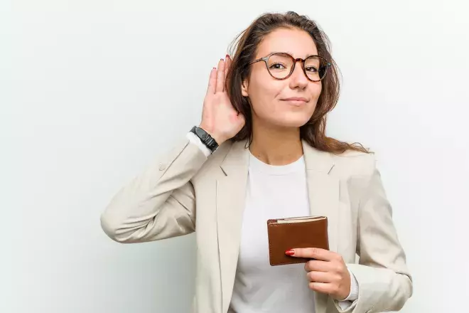 woman holding wallet holding hand up to ear to listen