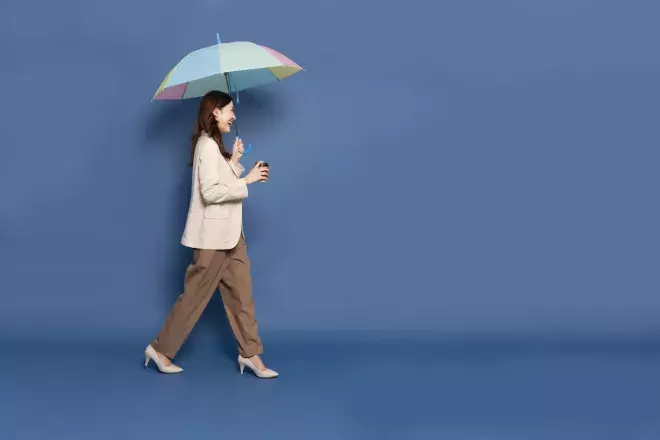 smiling business woman walking holding umbrella and coffee