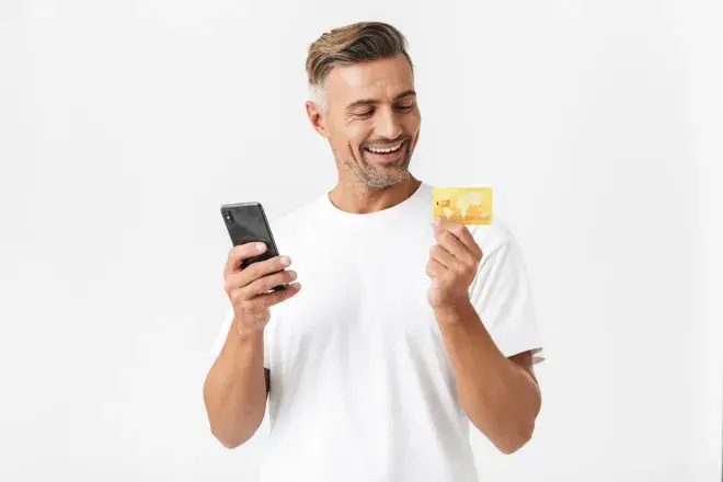 man smiling looking at credit card and holding phone