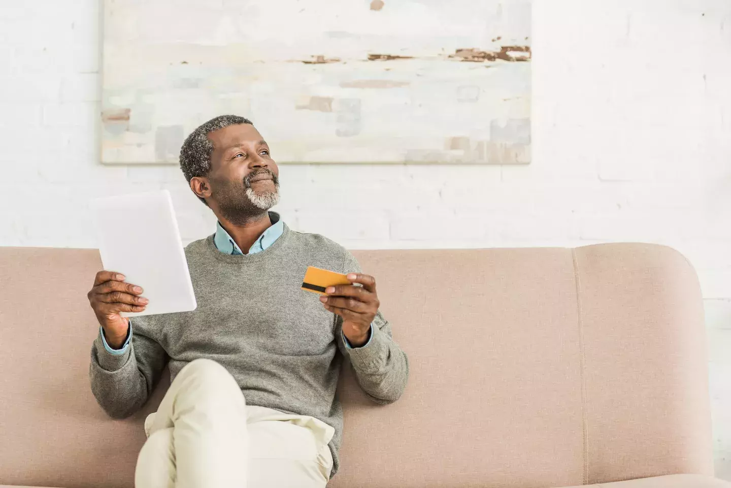 smiling man sitting on couch with credit card and phone