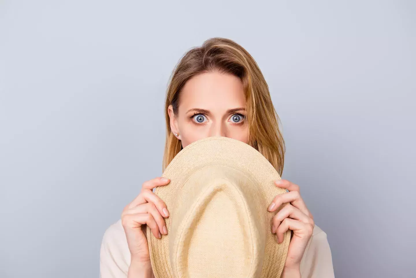 woman with shocked expression hiding behind hat