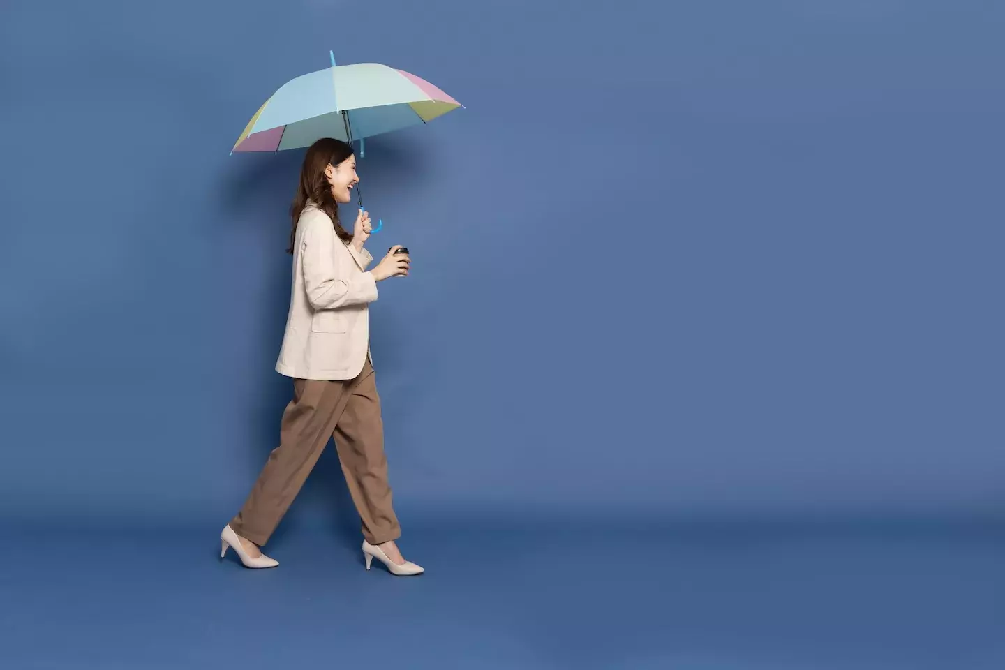 smiling business woman walking holding umbrella and coffee