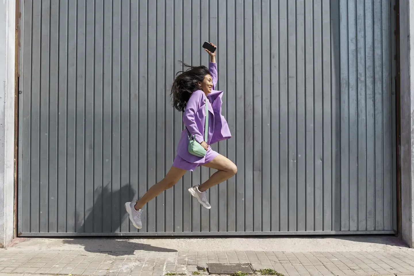 smiling woman leaping holding cell phone