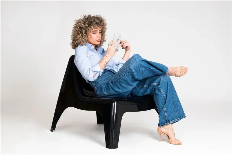 woman sitting cross legged in chair while reading phone