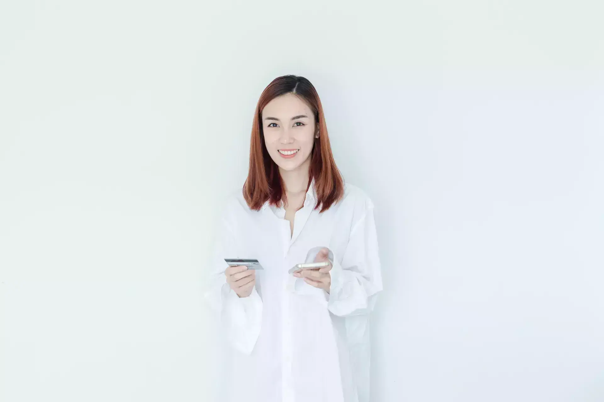Young woman in white shirt smiling while holding a phone and notepad.