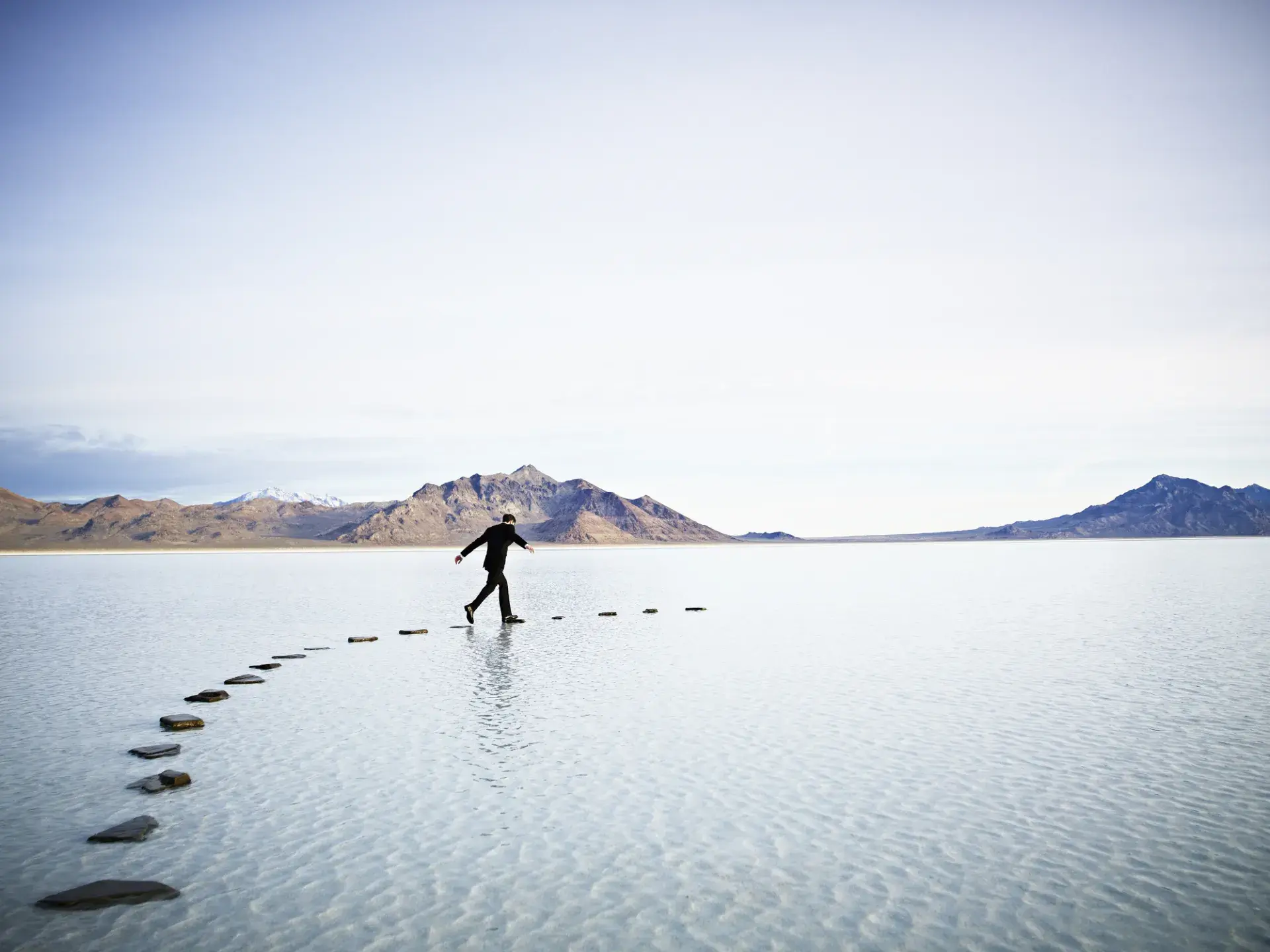 A person taking steps on a path of pebbles across a body of water.