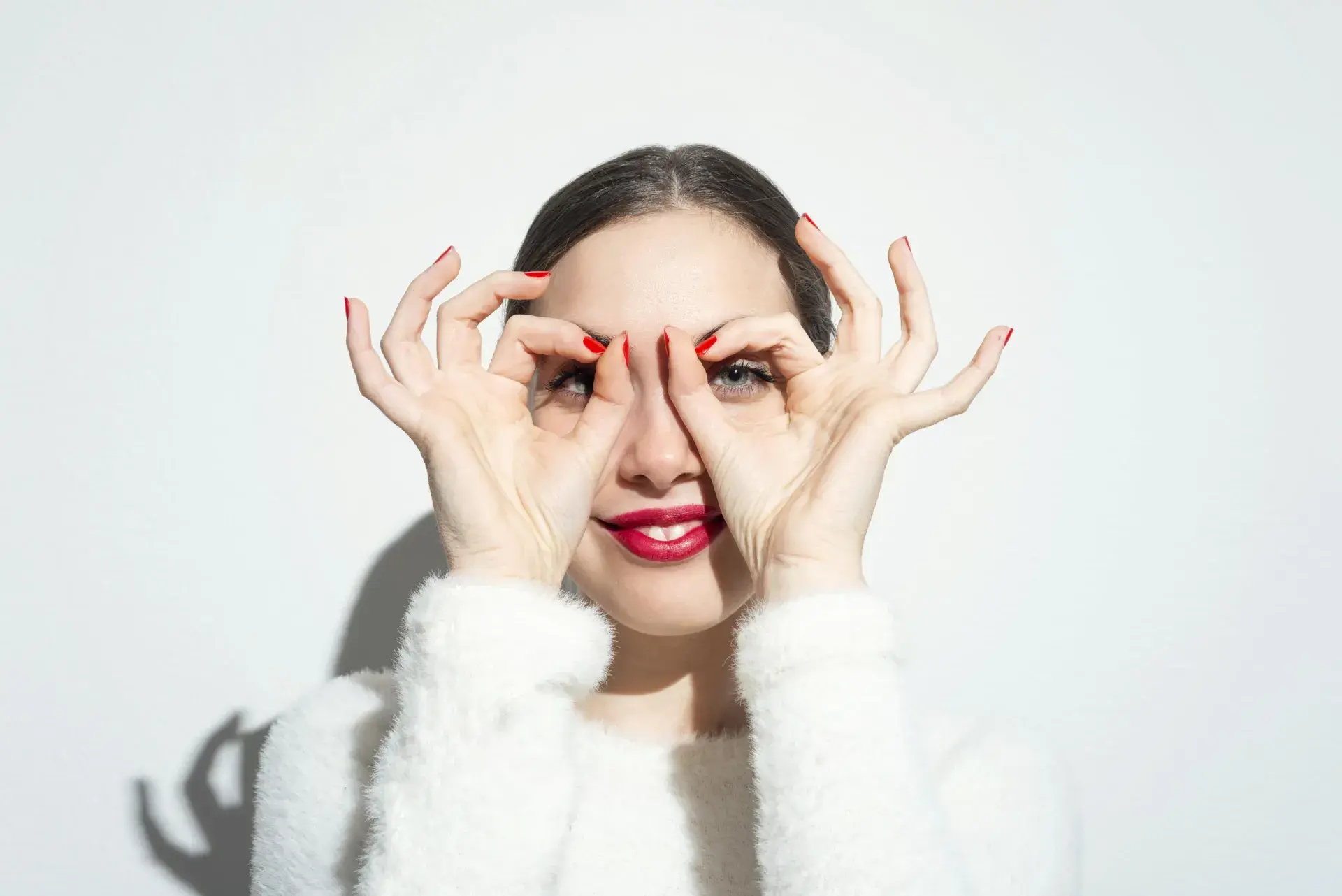 a woman with her fingers in the shape of circles over each of her eyes